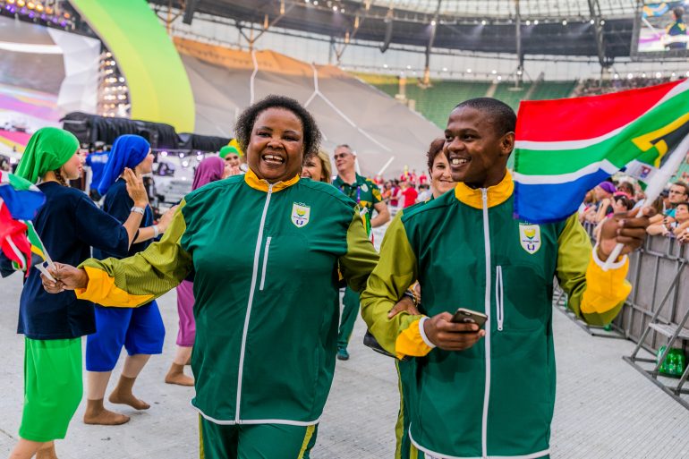 Photo of South African athletes walking and smiling while waving flags.
